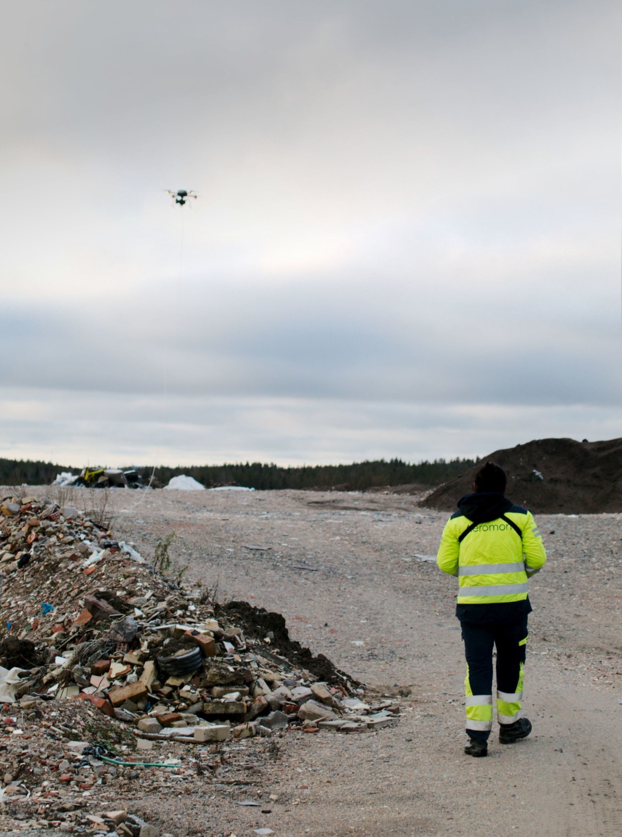 A drone flying above a landfill with a BH-12 device and a long sampling line.