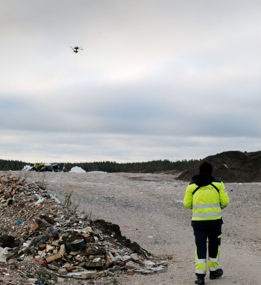 A drone flying above a landfill with a BH-12 device and a long sampling line.